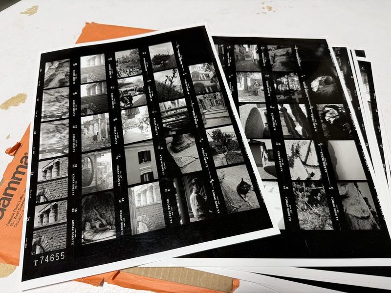 A stack of black and white proof sheets fanned out on an orange photo lab envelope