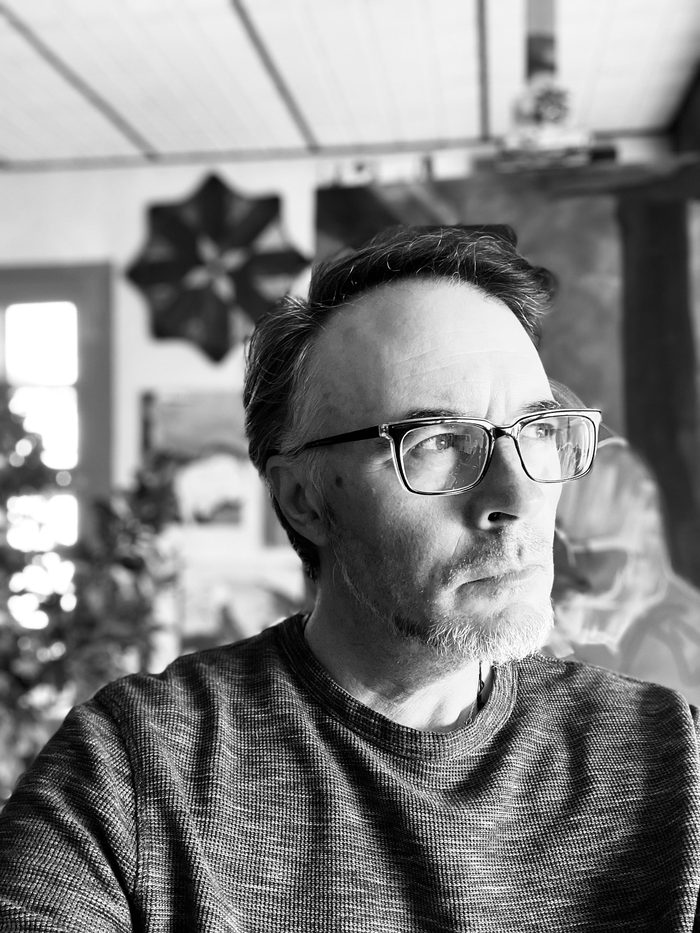 Black and white photograph of the artist in glasses, looking to the side, the source for the self-portrait